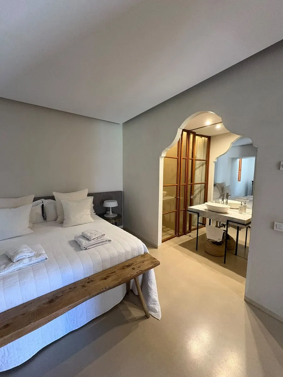 Doppelzimmer mit weißem Bett, Holzbank und offenem Bad